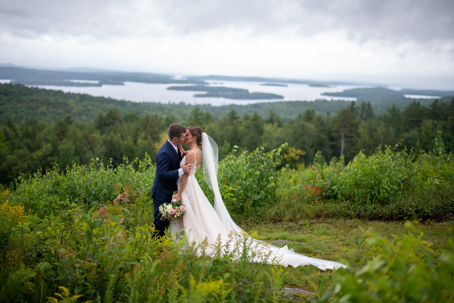 Bridget and Dave kissing high above a lake beneath a sweeping cloudy sky